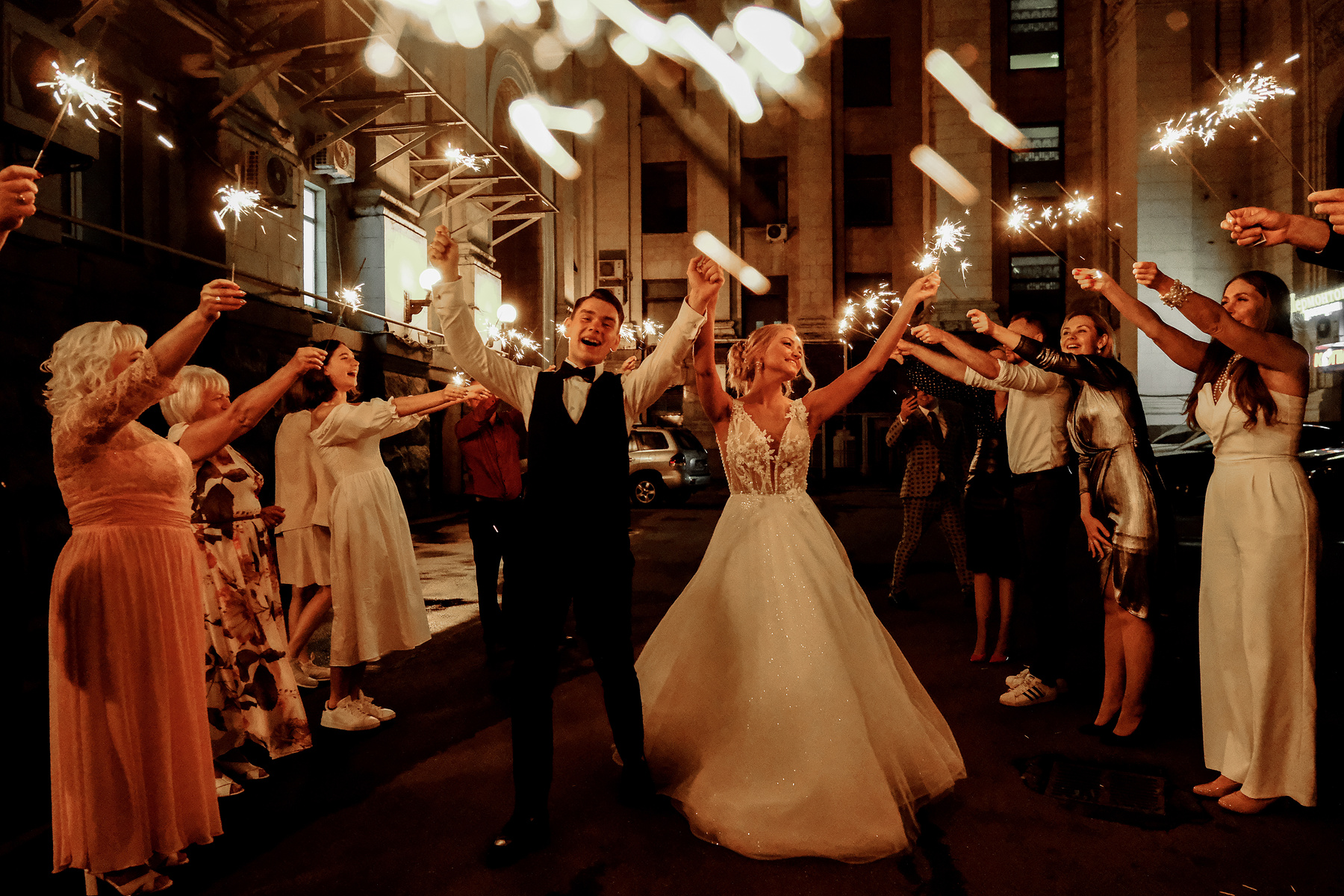 Happy friends and newlywed couple celebrating wedding at night